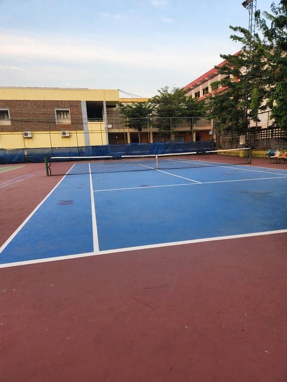 Blue hard court at Rungsang Tennis Courts with seating along the side