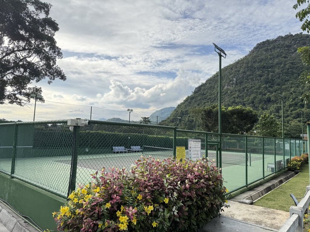 Fenced Che Elpend tennis court seen from the entrance path